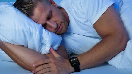 Ein Mann liegt schlafend im Bett und trägt dabei eine Pulsuhr zur Überwachung der Herzratenvariabilität zur Regeneration