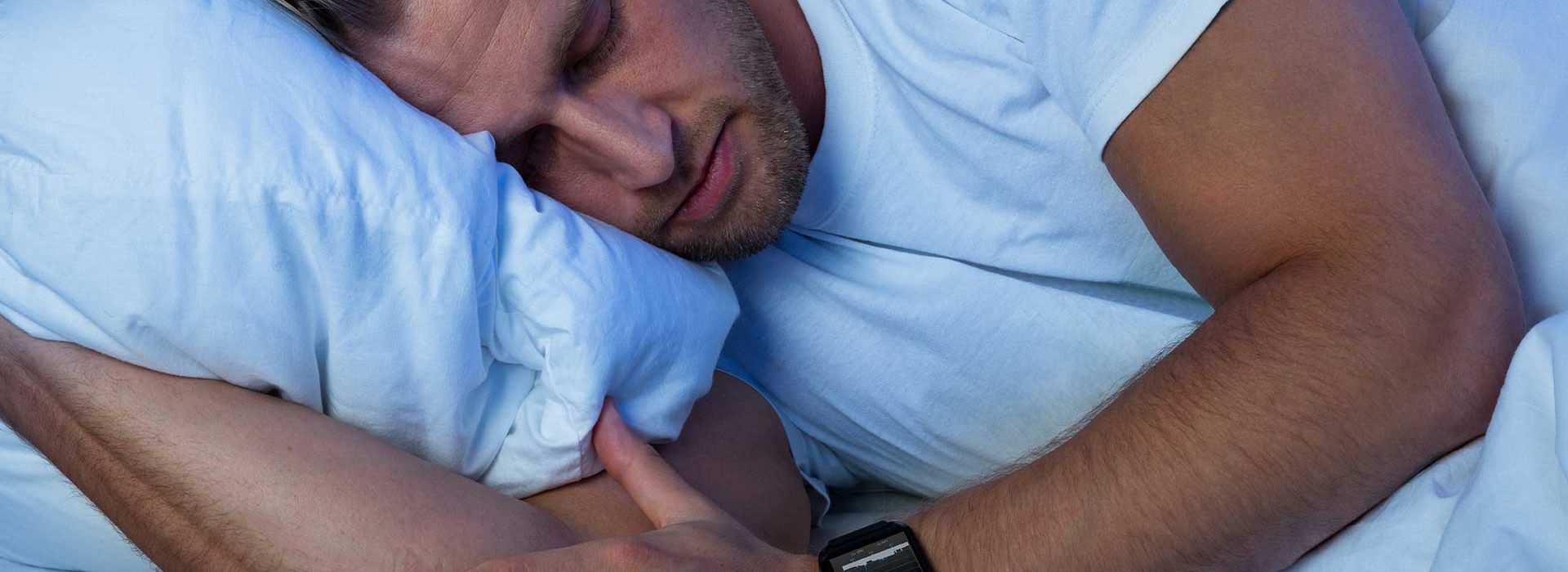 Ein Mann liegt schlafend im Bett und trägt dabei eine Pulsuhr zur Überwachung der Herzratenvariabilität zur Regeneration